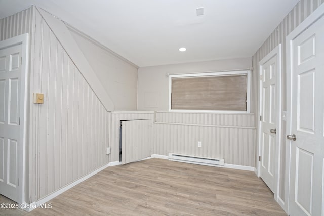 additional living space featuring a baseboard radiator, light wood-style floors, and a decorative wall