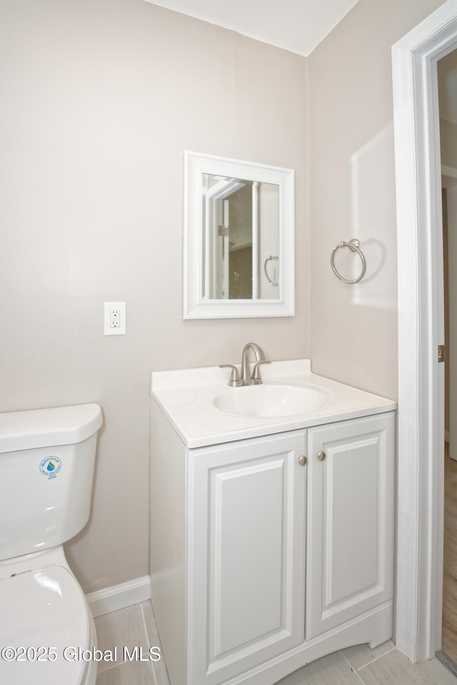 half bath featuring toilet, vanity, and baseboards