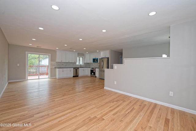 unfurnished living room with recessed lighting, light wood-type flooring, and baseboards