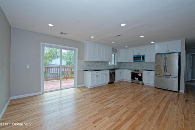 kitchen with appliances with stainless steel finishes, tasteful backsplash, light wood-style floors, a sink, and baseboards
