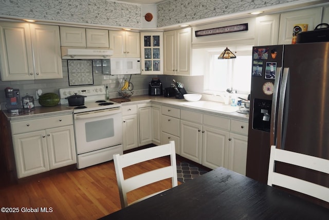 kitchen featuring white appliances, a sink, under cabinet range hood, light countertops, and backsplash