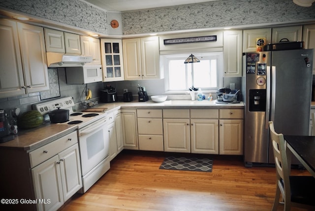 kitchen with white appliances, a sink, light wood finished floors, under cabinet range hood, and backsplash