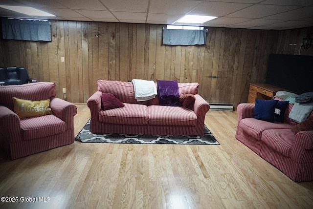 living area with a drop ceiling, a baseboard heating unit, wood finished floors, and wood walls