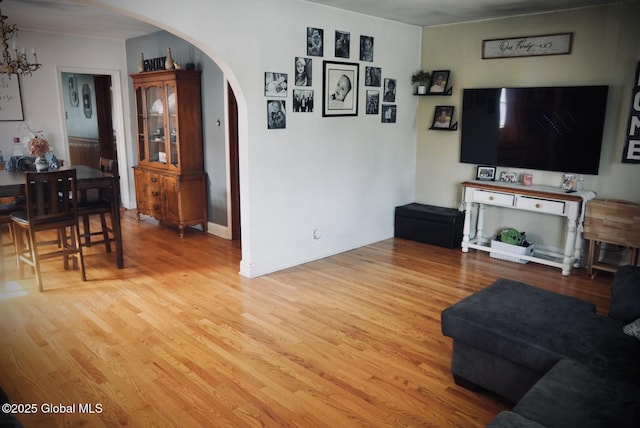 living room featuring arched walkways, light wood-style flooring, baseboards, and a chandelier