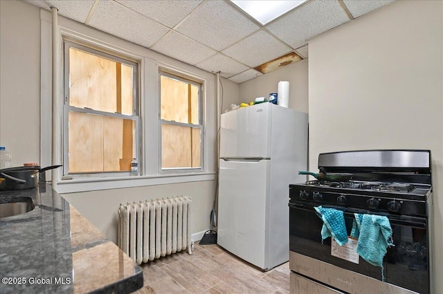 kitchen featuring radiator, gas range, freestanding refrigerator, a drop ceiling, and light wood-style flooring
