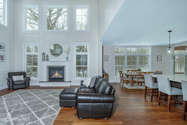 living room with a high ceiling, dark wood-type flooring, a glass covered fireplace, and recessed lighting
