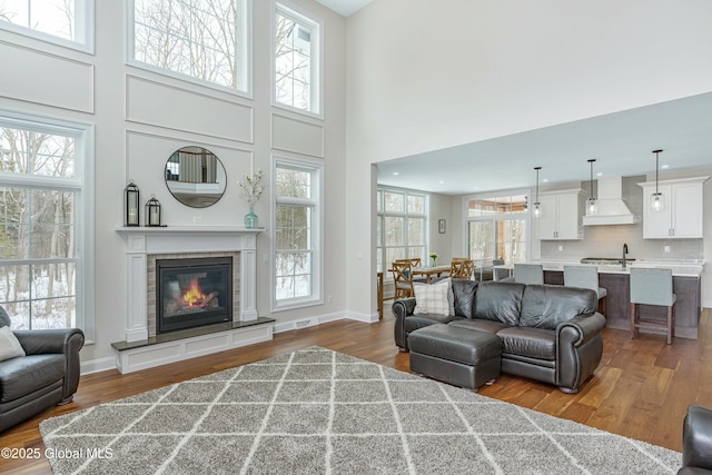 living room featuring wood finished floors, a high ceiling, a glass covered fireplace, and baseboards
