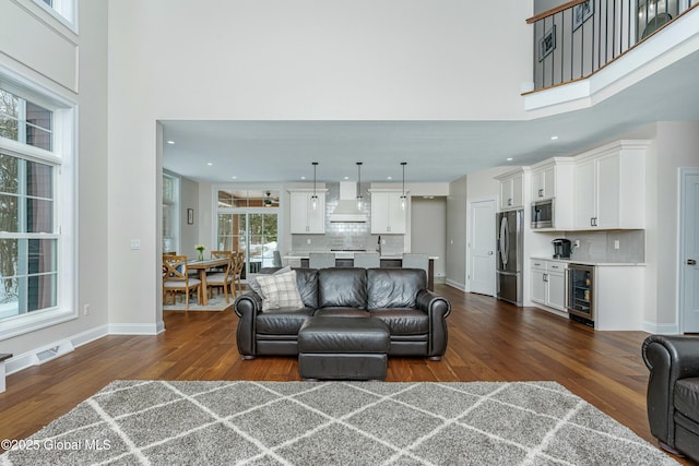 living area with beverage cooler, dark wood-type flooring, a towering ceiling, recessed lighting, and baseboards