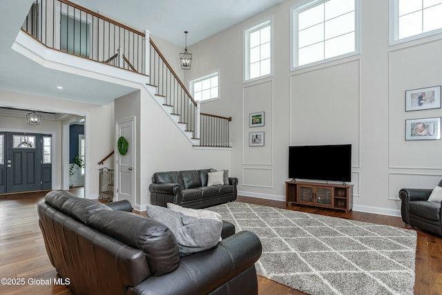 living room with a towering ceiling, stairs, plenty of natural light, wood finished floors, and baseboards