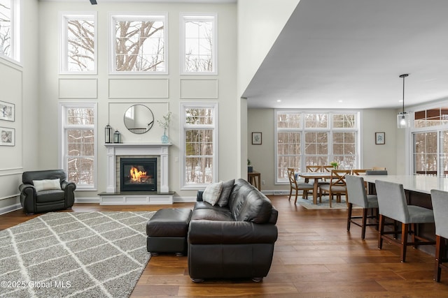 living area featuring wood finished floors, a towering ceiling, and a glass covered fireplace