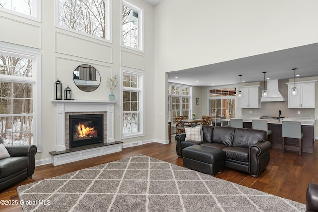 living area with a towering ceiling, a glass covered fireplace, dark wood-style floors, and plenty of natural light