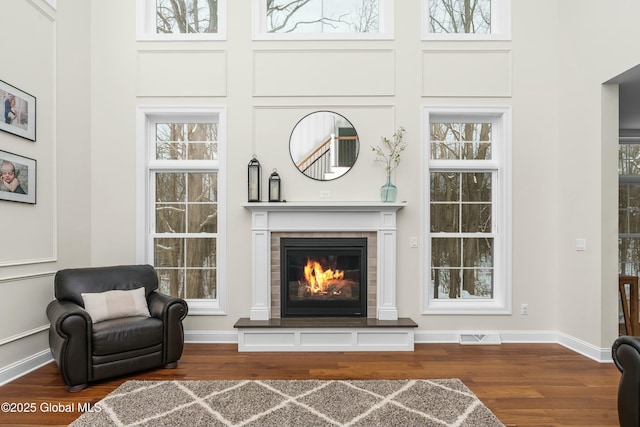 sitting room with wood finished floors, a fireplace, baseboards, and a high ceiling