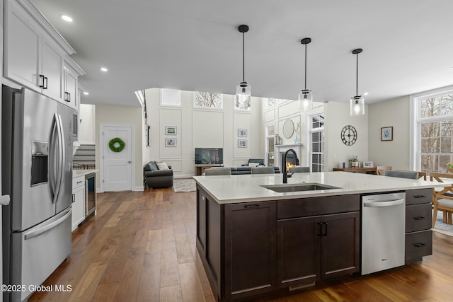 kitchen featuring appliances with stainless steel finishes, a sink, beverage cooler, dark wood-style floors, and dark brown cabinets