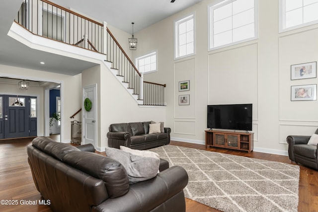 living room with a high ceiling, stairs, healthy amount of natural light, wood finished floors, and baseboards
