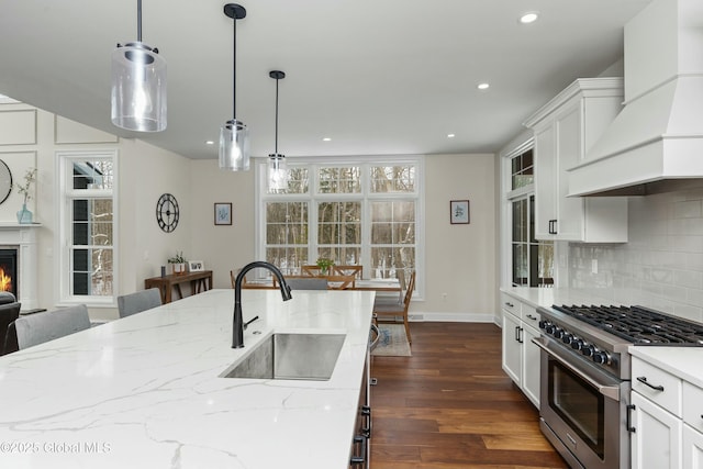 kitchen featuring stainless steel range, a sink, premium range hood, a kitchen breakfast bar, and decorative backsplash