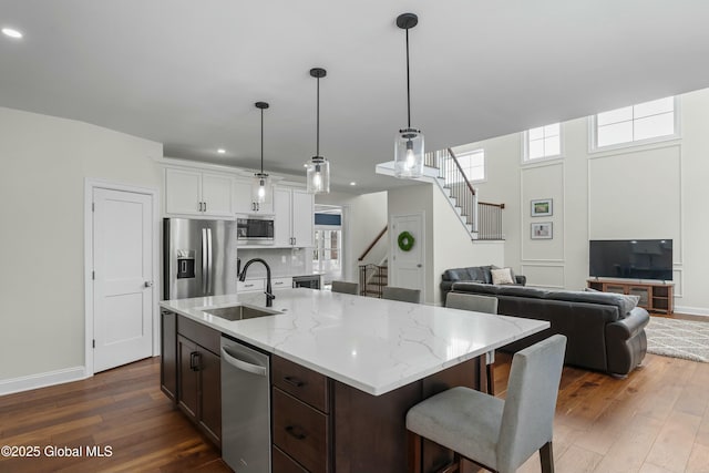 kitchen with a sink, appliances with stainless steel finishes, dark wood-style flooring, open floor plan, and baseboards