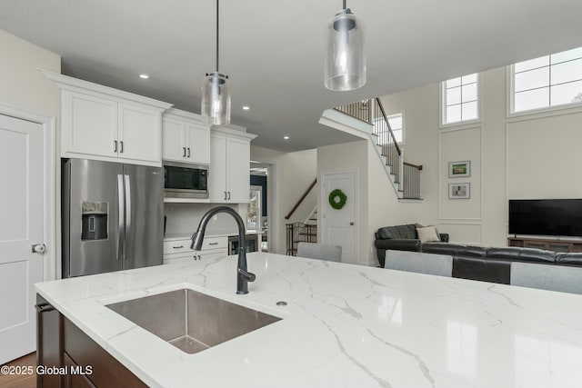 kitchen with stainless steel appliances, a sink, open floor plan, decorative light fixtures, and white cabinetry