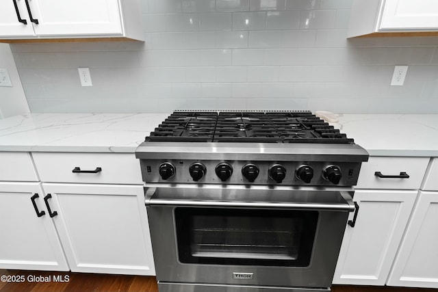 kitchen featuring high end range, white cabinetry, decorative backsplash, and light stone countertops