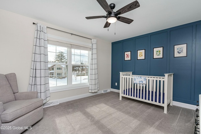 carpeted bedroom featuring multiple windows, baseboards, a decorative wall, a crib, and ceiling fan