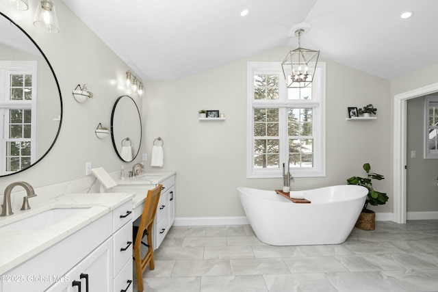 bathroom with marble finish flooring, a chandelier, two vanities, lofted ceiling, and a freestanding tub