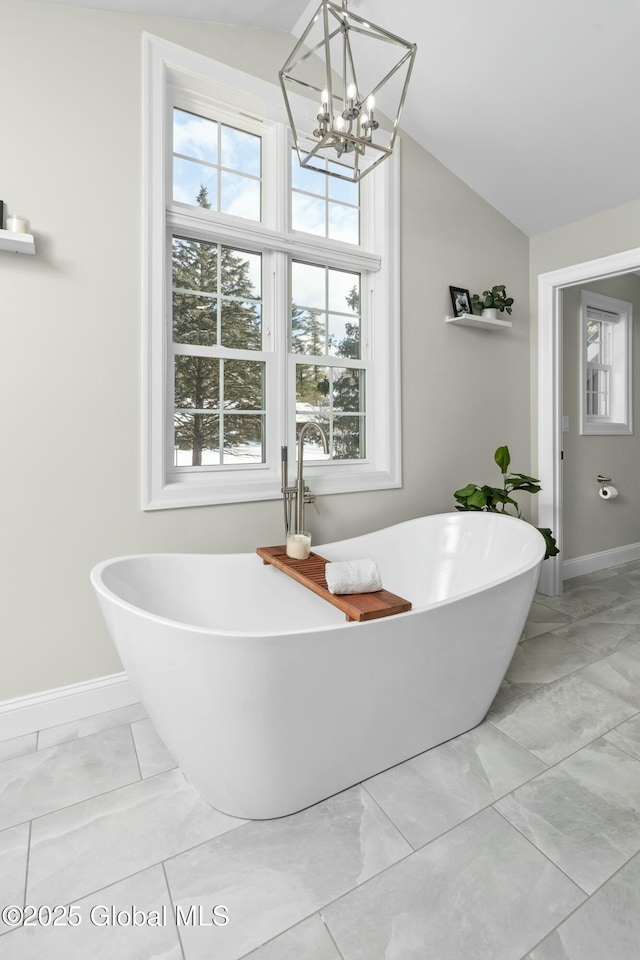 bathroom featuring marble finish floors, baseboards, a chandelier, vaulted ceiling, and a freestanding bath