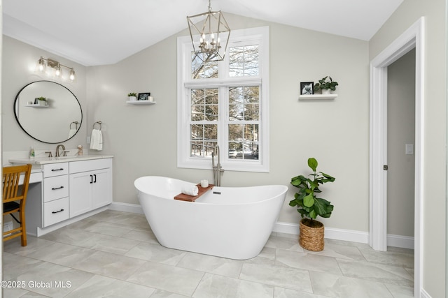 full bathroom featuring vaulted ceiling, a chandelier, vanity, a freestanding bath, and baseboards
