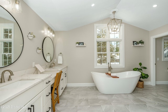 full bathroom with a chandelier, marble look tiles, a freestanding tub, two vanities, and vaulted ceiling