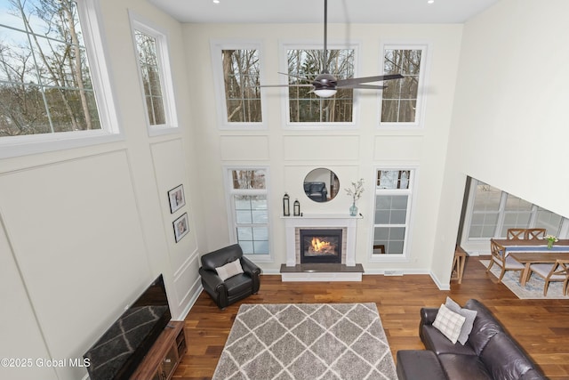 living room featuring a towering ceiling, ceiling fan, wood finished floors, and a glass covered fireplace