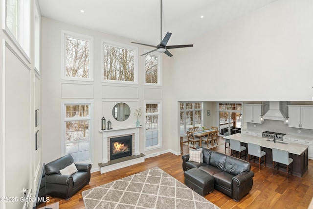 living room with a towering ceiling, ceiling fan, plenty of natural light, a glass covered fireplace, and recessed lighting