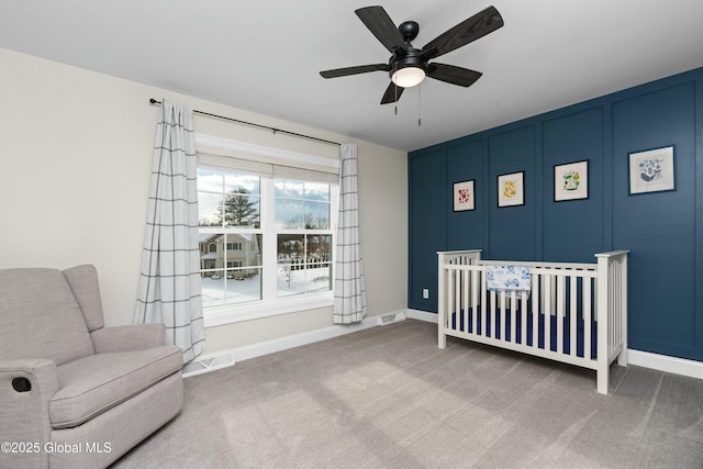 bedroom featuring a crib, carpet floors, baseboards, a decorative wall, and a ceiling fan