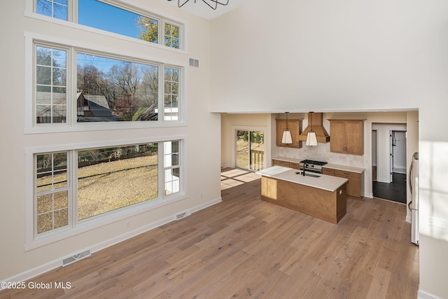 kitchen featuring a high ceiling, light wood-type flooring, brown cabinets, light countertops, and a center island with sink