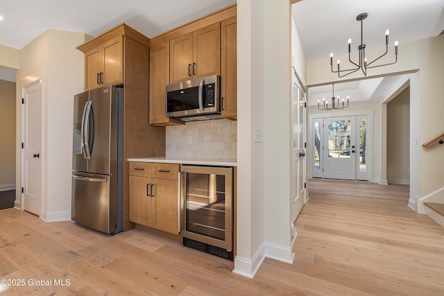 kitchen with appliances with stainless steel finishes, wine cooler, a chandelier, decorative backsplash, and light wood-style floors