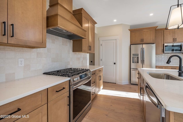 kitchen featuring stainless steel appliances, premium range hood, a sink, light wood-type flooring, and brown cabinetry
