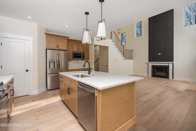 kitchen with appliances with stainless steel finishes, a sink, baseboards, light wood finished floors, and pendant lighting