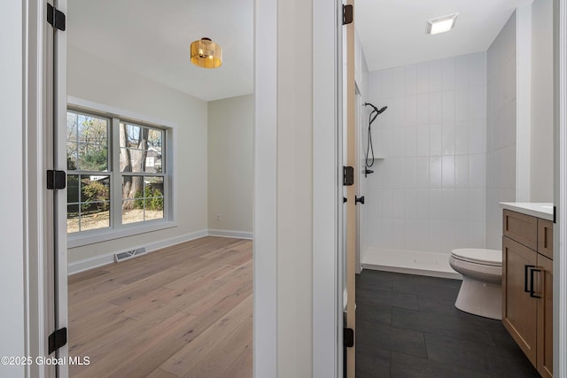 full bath with vanity, tiled shower, toilet, wood finished floors, and baseboards