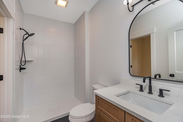 bathroom with toilet, tiled shower, and vanity