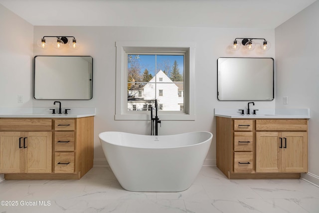 full bath featuring marble look tiles, a freestanding bath, two vanities, and baseboards