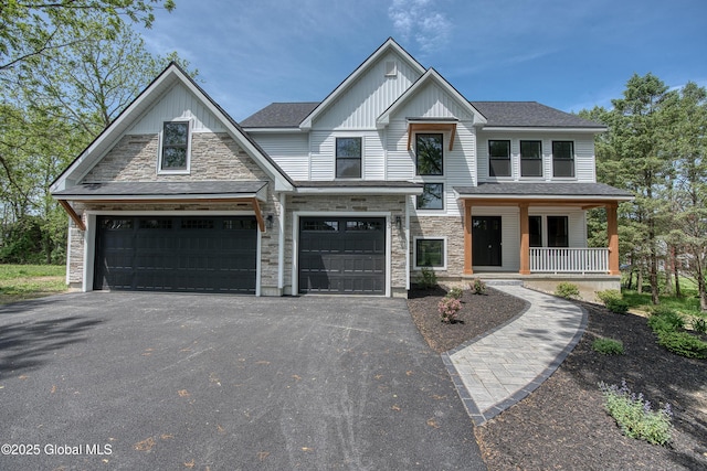 view of front facade featuring board and batten siding, driveway, stone siding, covered porch, and a garage