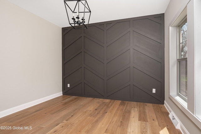 unfurnished room featuring a chandelier, light wood-type flooring, and baseboards