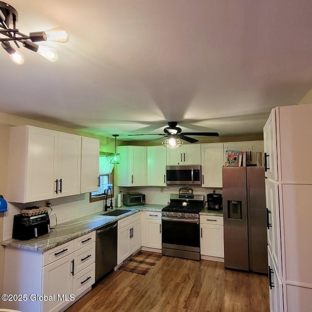 kitchen featuring stainless steel appliances, a sink, white cabinetry, dark wood finished floors, and backsplash