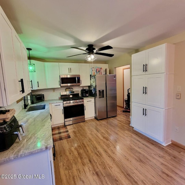 kitchen featuring stainless steel appliances, a sink, light wood-type flooring, white cabinets, and light stone counters
