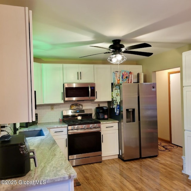 kitchen featuring stainless steel appliances, backsplash, a ceiling fan, white cabinetry, and light wood-style flooring
