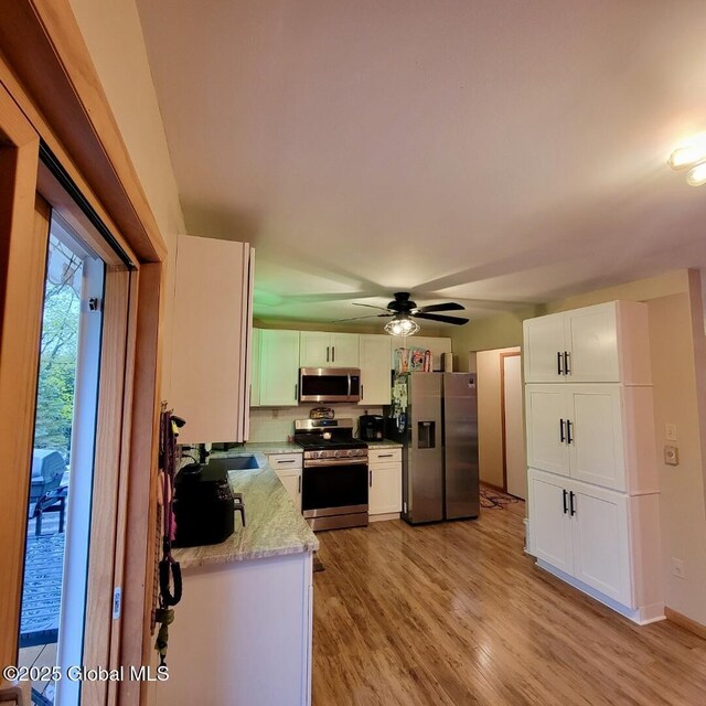 kitchen with appliances with stainless steel finishes, white cabinets, light wood finished floors, and ceiling fan