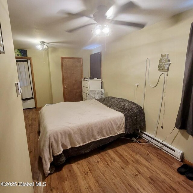 bedroom with baseboard heating, wood finished floors, and a ceiling fan