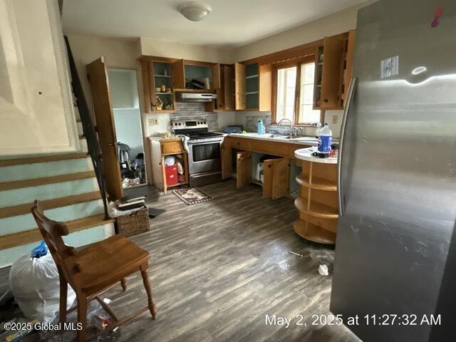 kitchen with stainless steel appliances, under cabinet range hood, light countertops, dark wood-style floors, and brown cabinetry