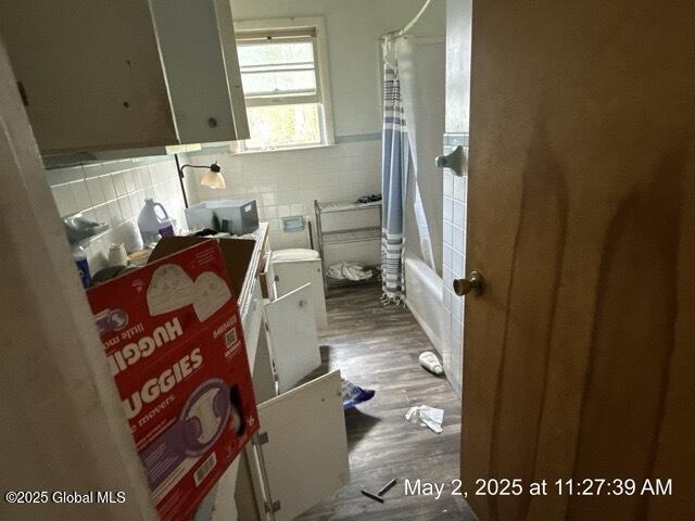 full bath featuring tile walls, wood finished floors, and wainscoting