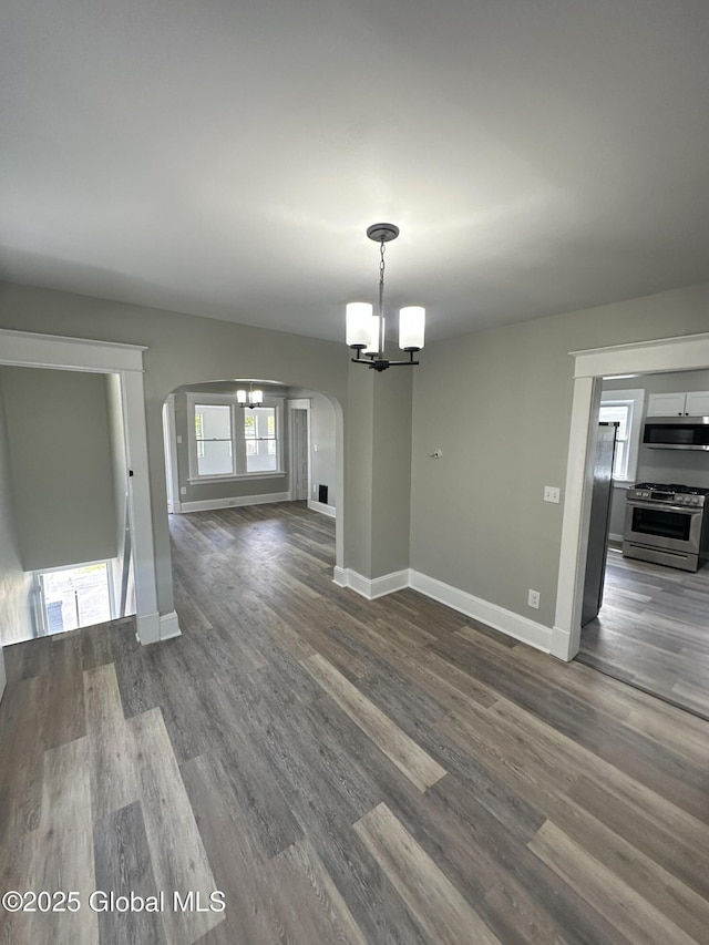 unfurnished dining area featuring arched walkways, a chandelier, baseboards, and dark wood-type flooring