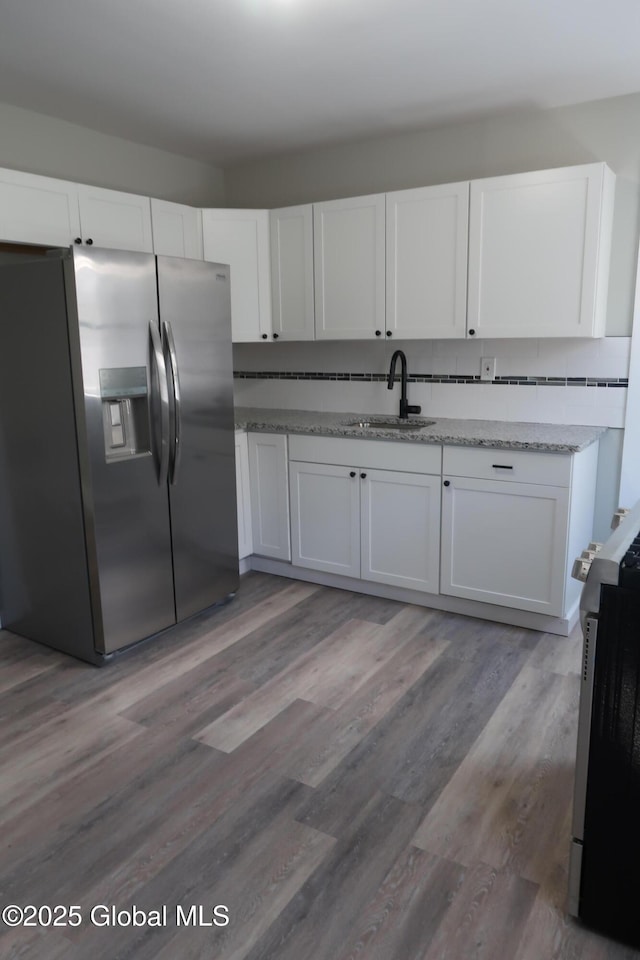kitchen with appliances with stainless steel finishes, a sink, white cabinets, and light stone counters