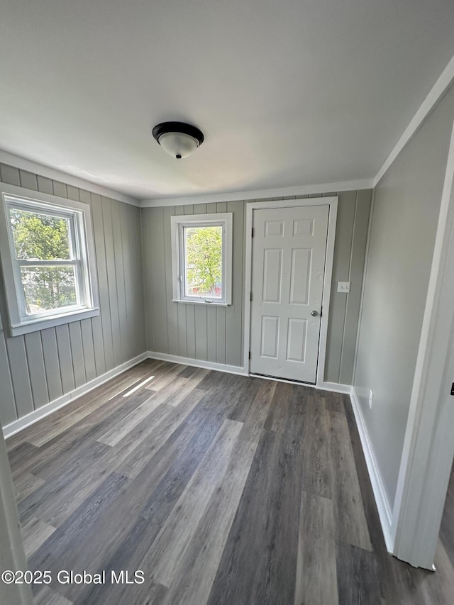 unfurnished bedroom featuring wood finished floors, multiple windows, baseboards, and ornamental molding