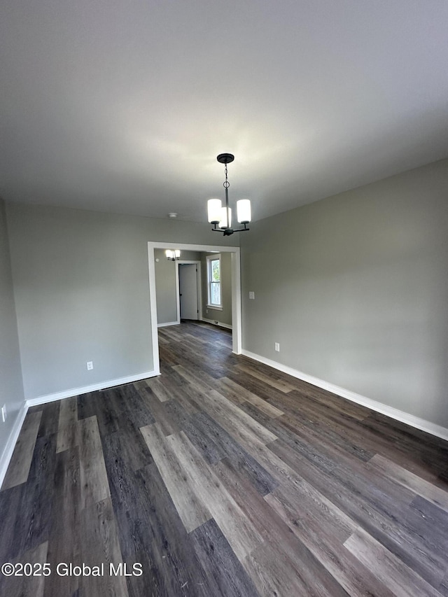 unfurnished dining area with a chandelier, dark wood finished floors, and baseboards